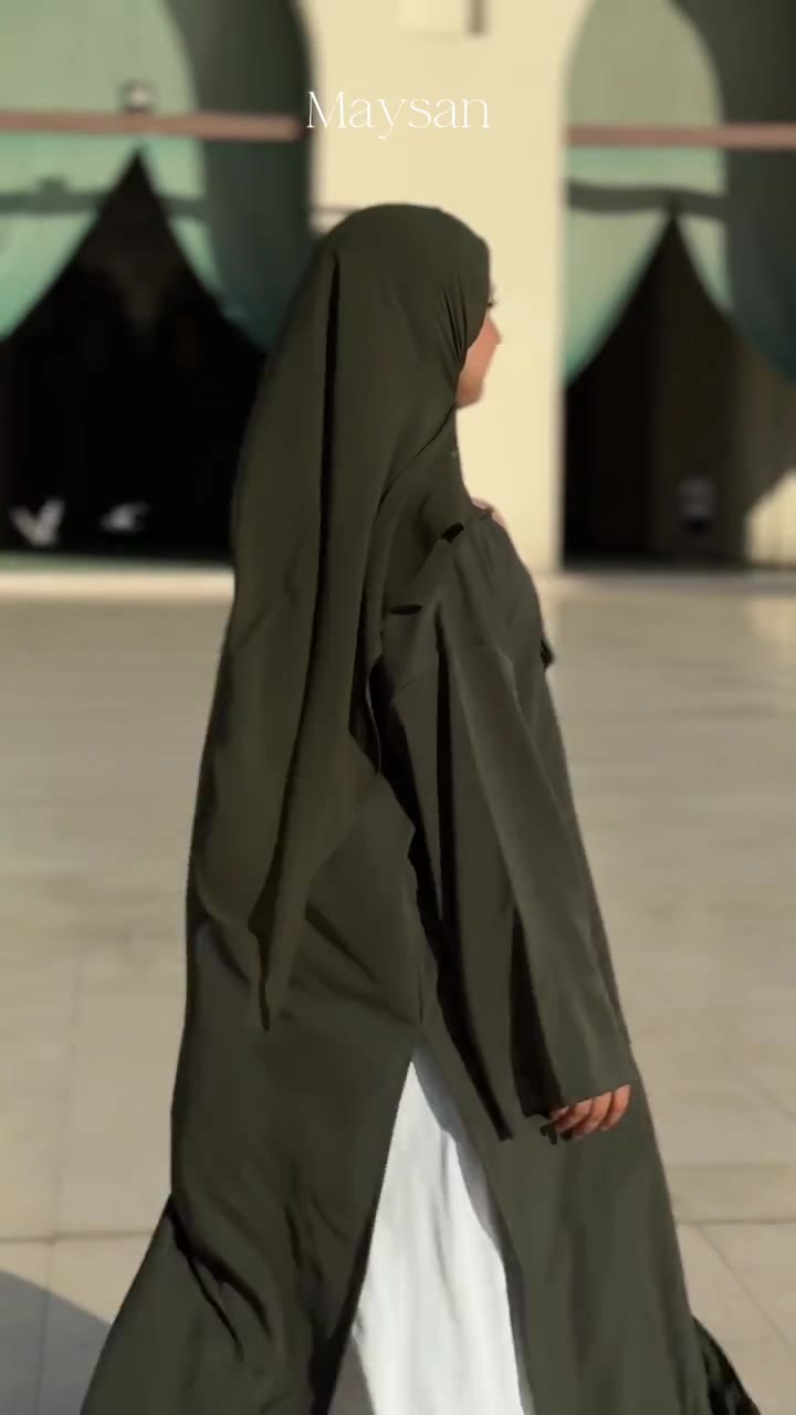 A woman in an olive abaya walking through a mosque courtyard